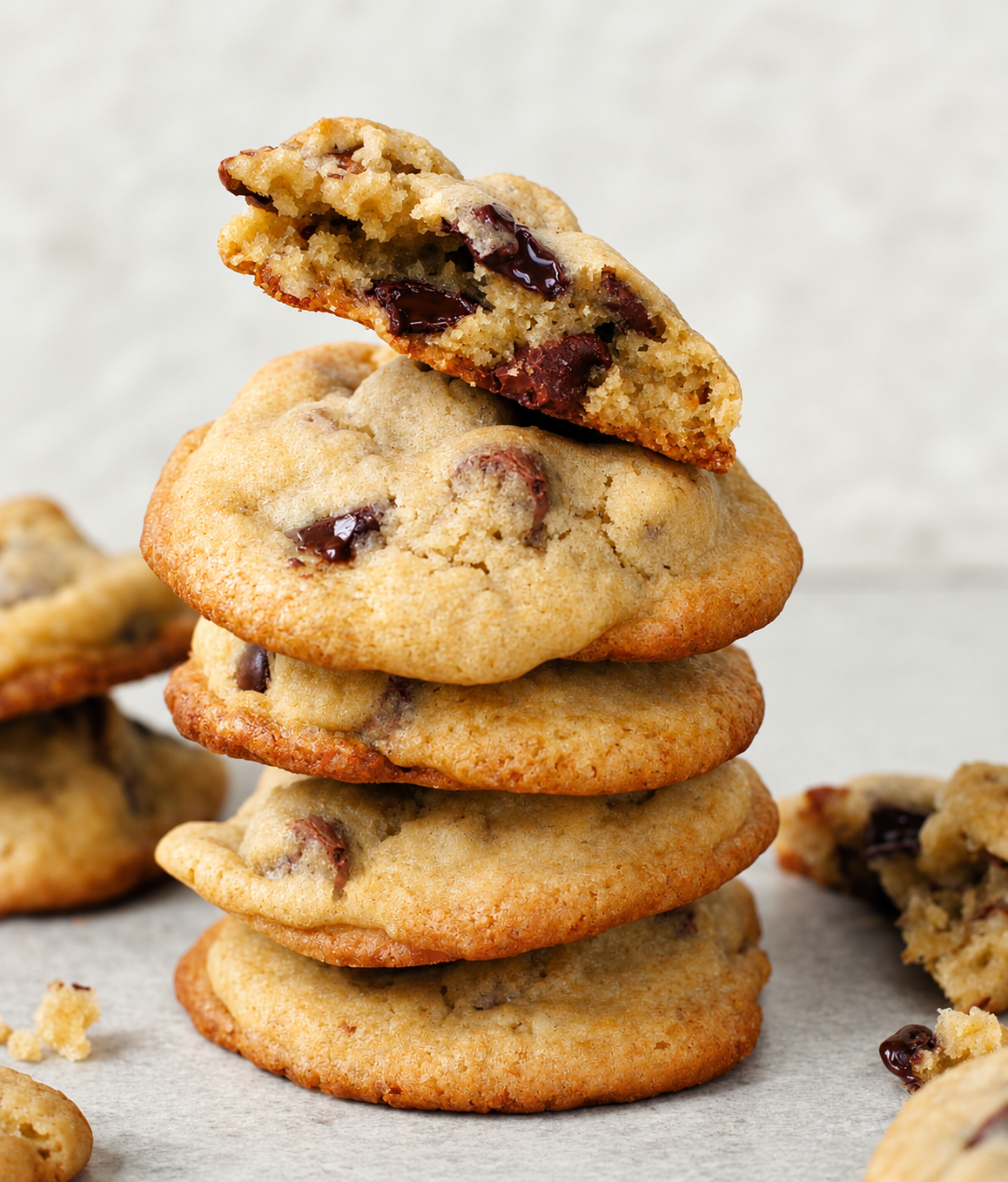 A tall stack of freshly baked chocolate chip cookies with one broken in half on top